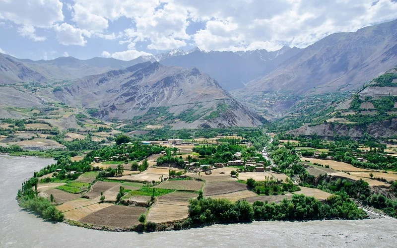 green grass field near lake and mountains during daytime near pamir highway afghanistan