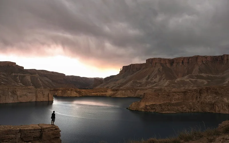 person standing on rock formation near lake under cloudy sky during daytime at band e amir afghanistan




